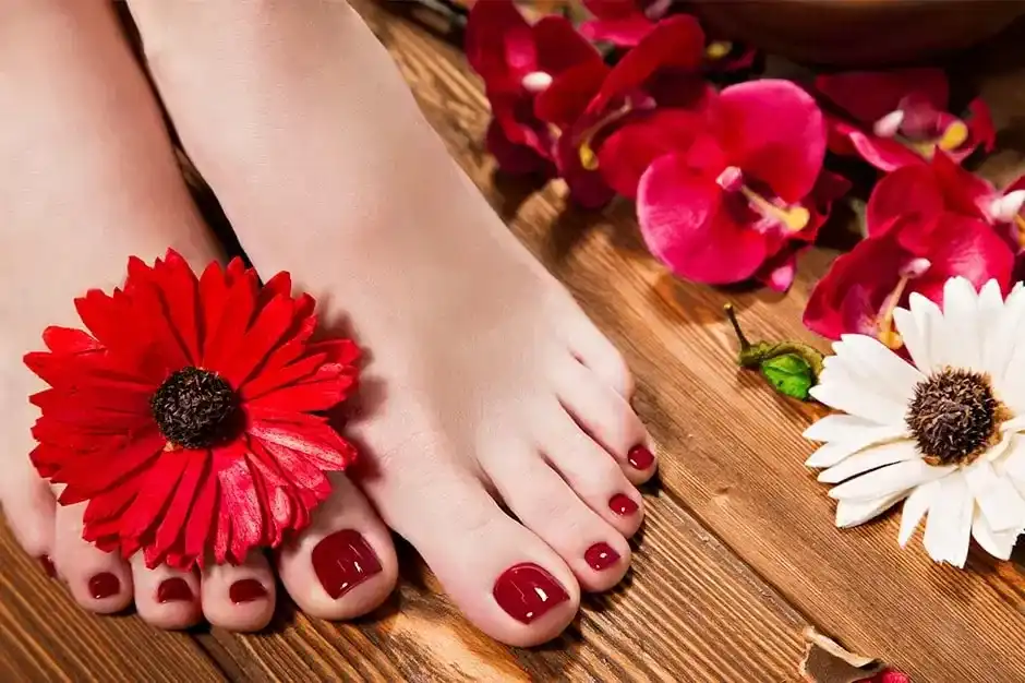 Red-painted toenails with flowers on a wooden floor, surrounded by red and white blooms.