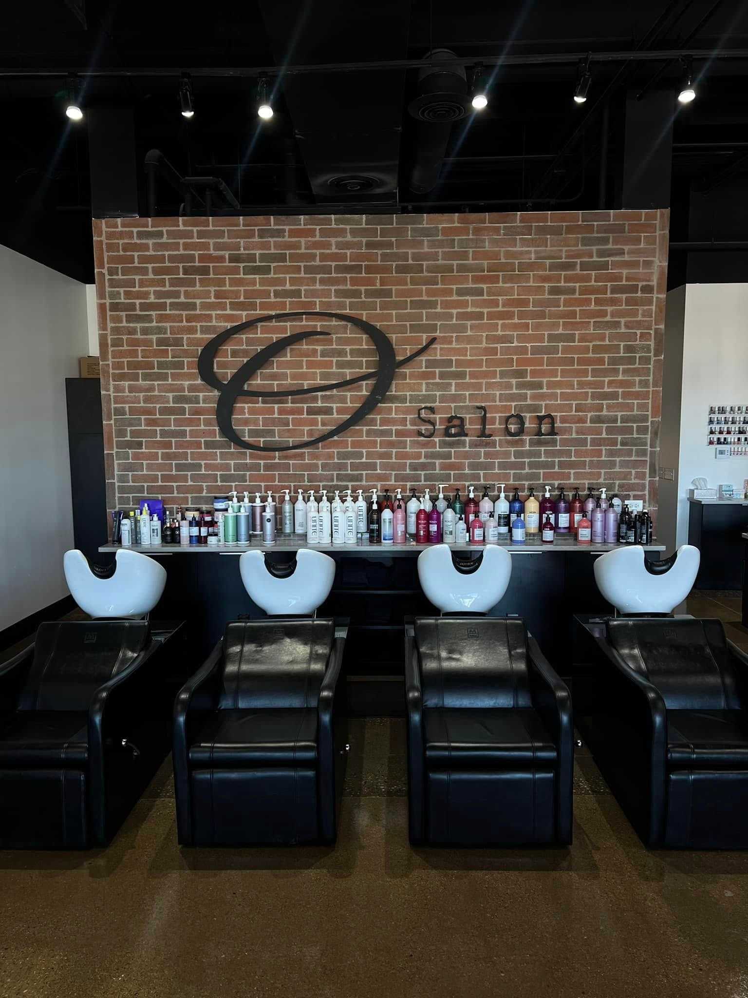 Four salon hair-washing stations with product shelves against a brick wall and "Salon" sign.