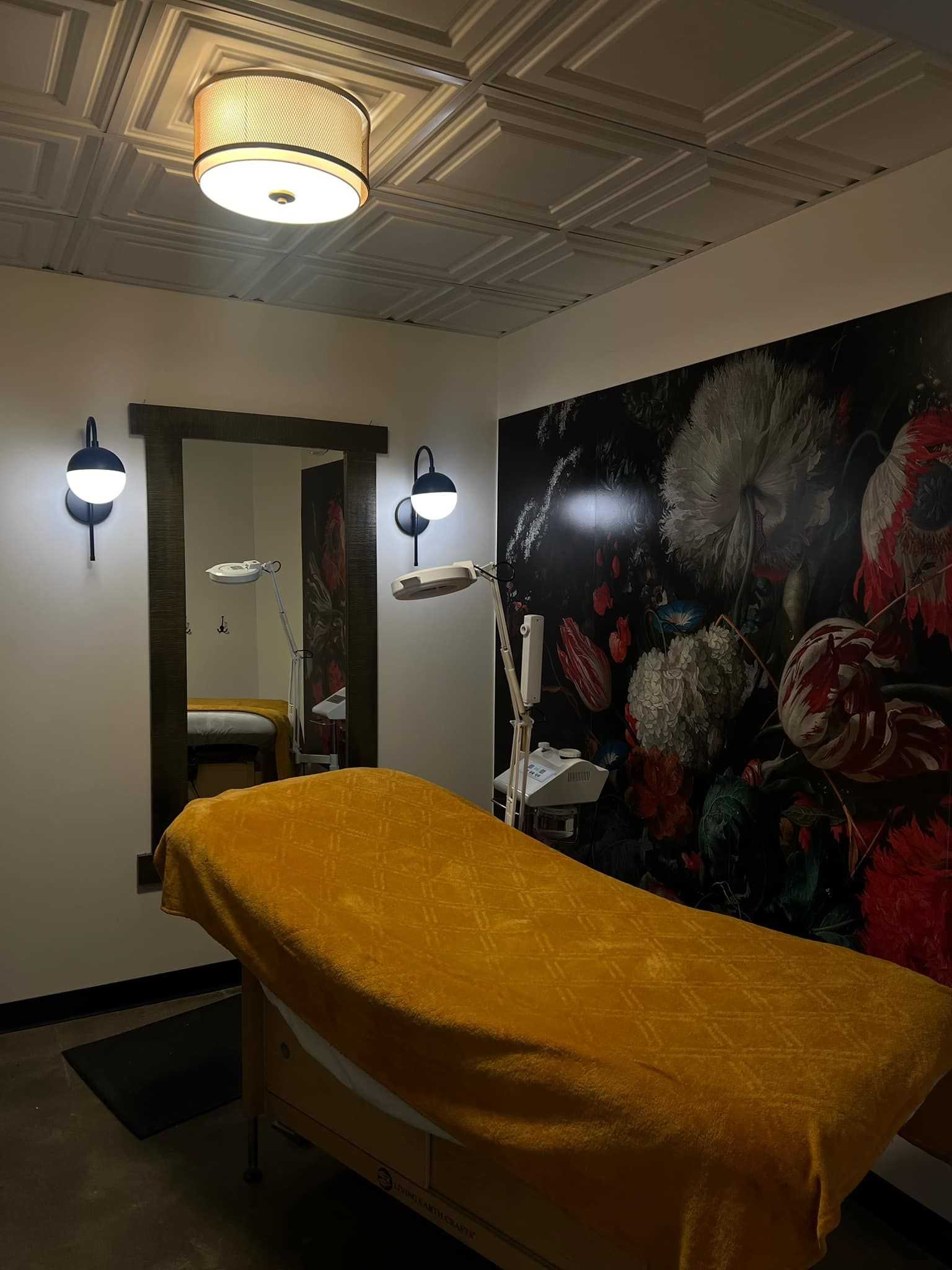 Aesthetic treatment room with a yellow-covered bed, floral mural, and soft lighting.